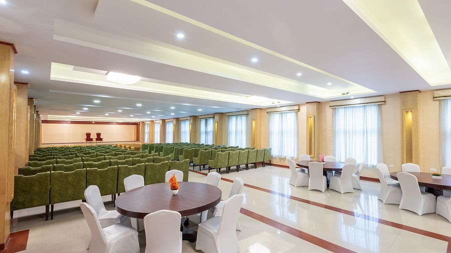 A side angle shot of a banquet hall at DLS Tehri Club Resort featuring green sofas and round table.